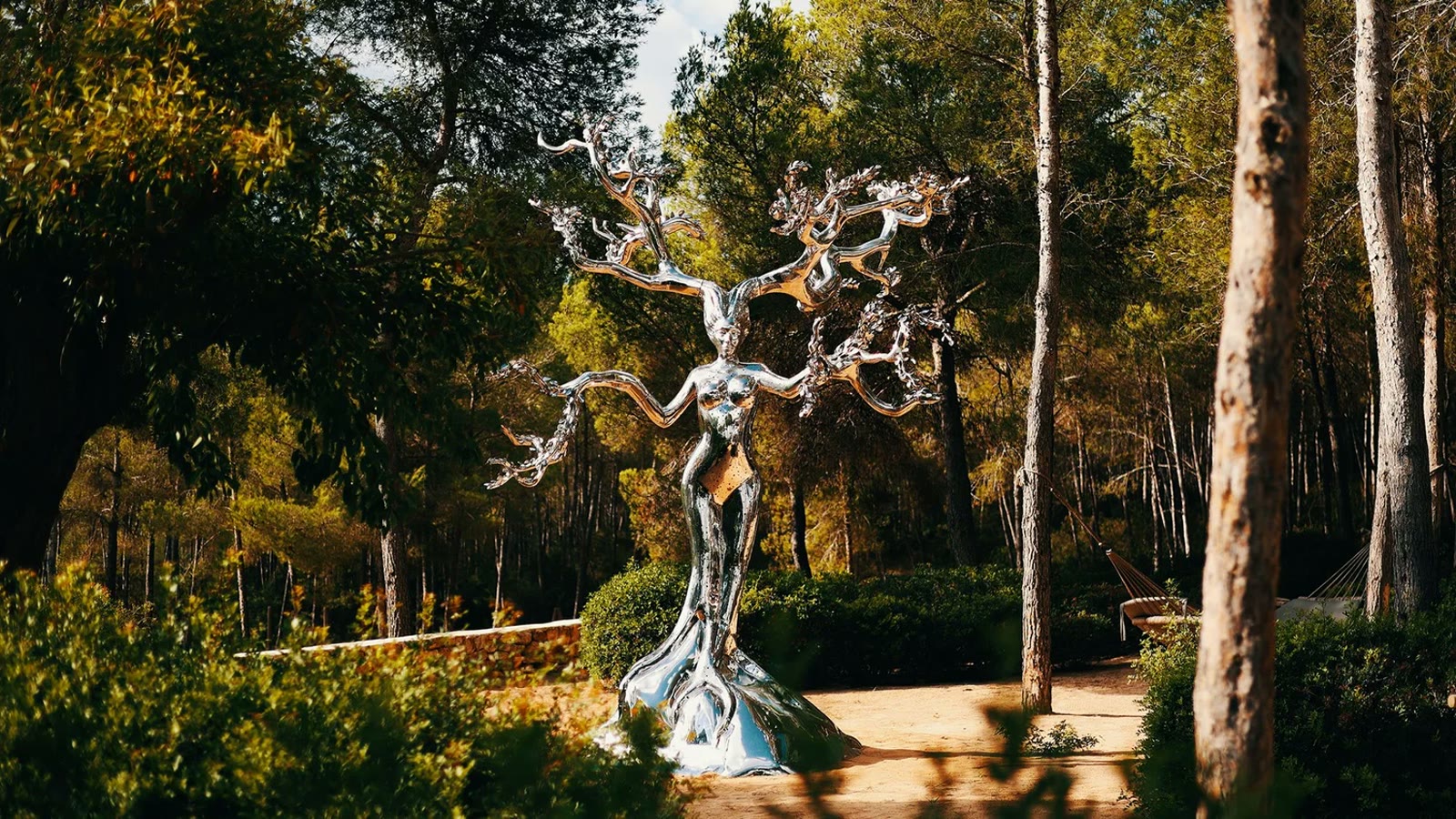 A mirror-polished tree sculpture in a sunlit forest