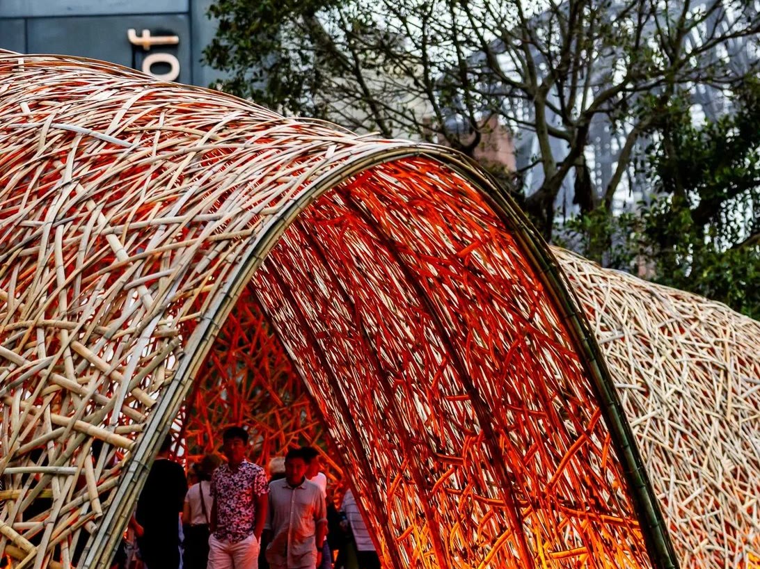 Glowing woven bamboo tunnel pavilion with people walking through